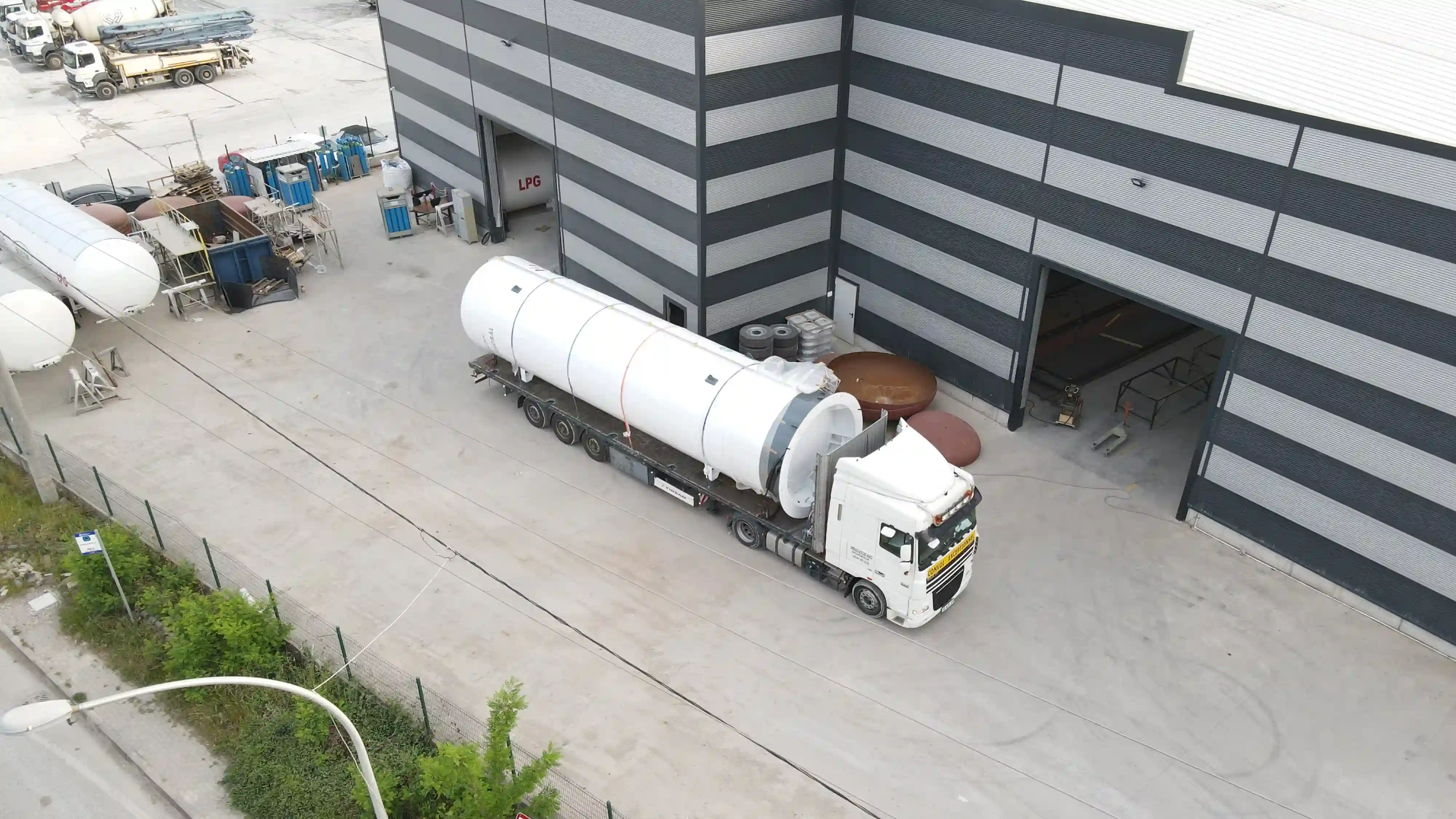 Fabrika sahasında ağır vasıta tır üzerine yüklenmiş, sevkiyata hazır yatay LNG (Sıvılaştırılmış Doğal Gaz) depolama tankı drone çekimi.