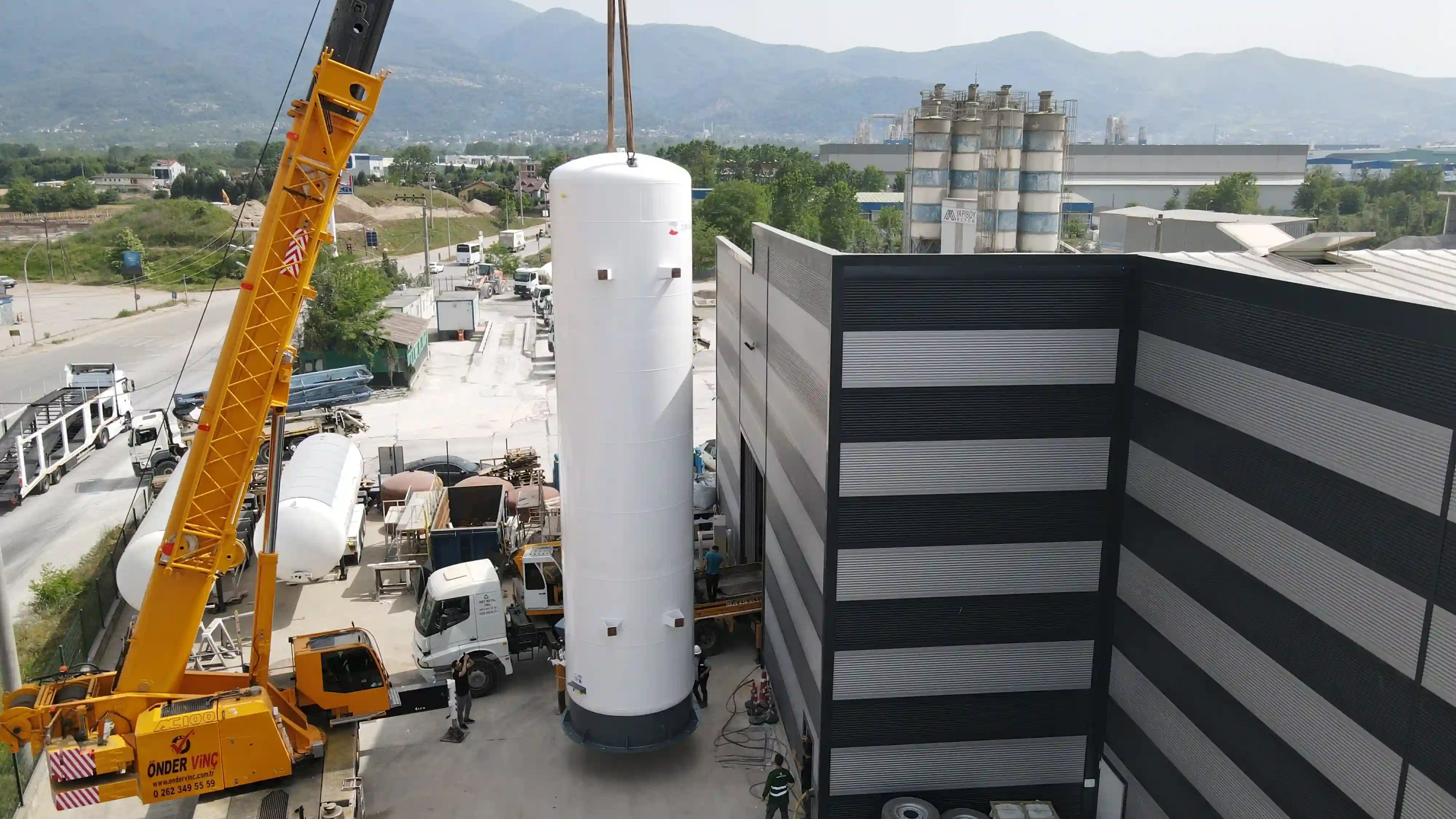 Fabrika alanında ağır tonajlı vinç ile dikey olarak konumlandırılan, yüksek kapasiteli kriyojenik LNG depolama tankı drone görünümü.